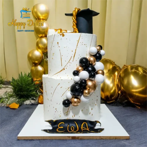 Two-tier graduation cake in black, white, and gold with cap topper and balloon decor