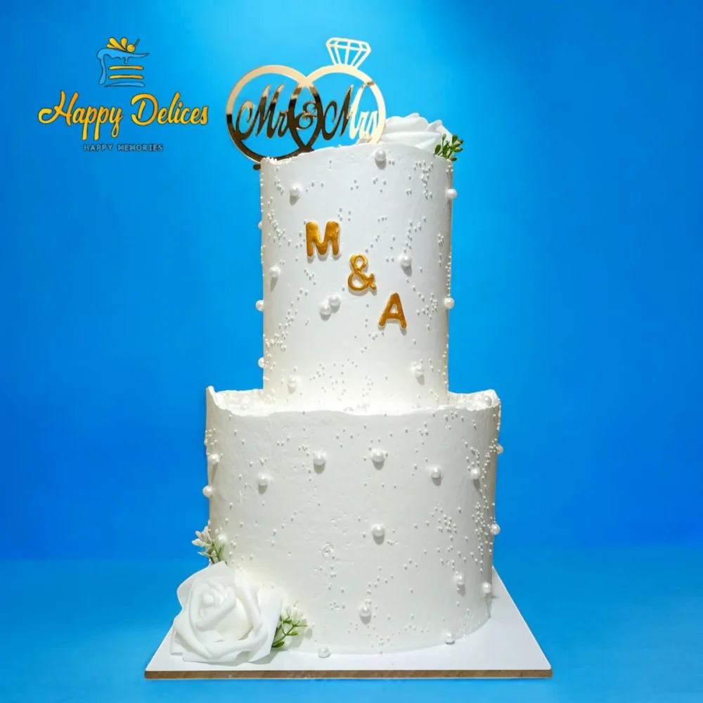 Elegant white two-tier wedding cake with pearl details and initials M&A by Happy Delices