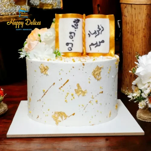 White and gold celebration cake with an open book topper and floral accents by Happy Delices