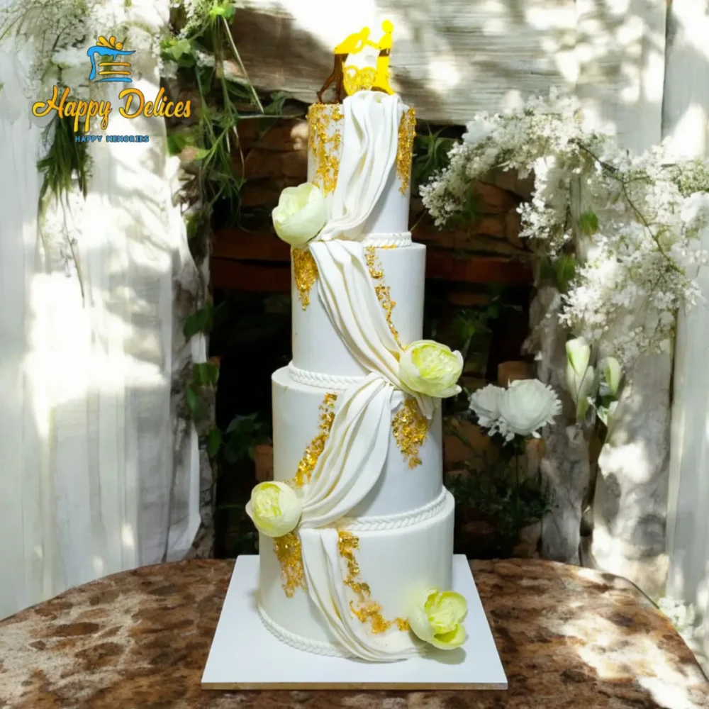 Three-tier elegant white wedding cake with gold leaf and flowing drapes