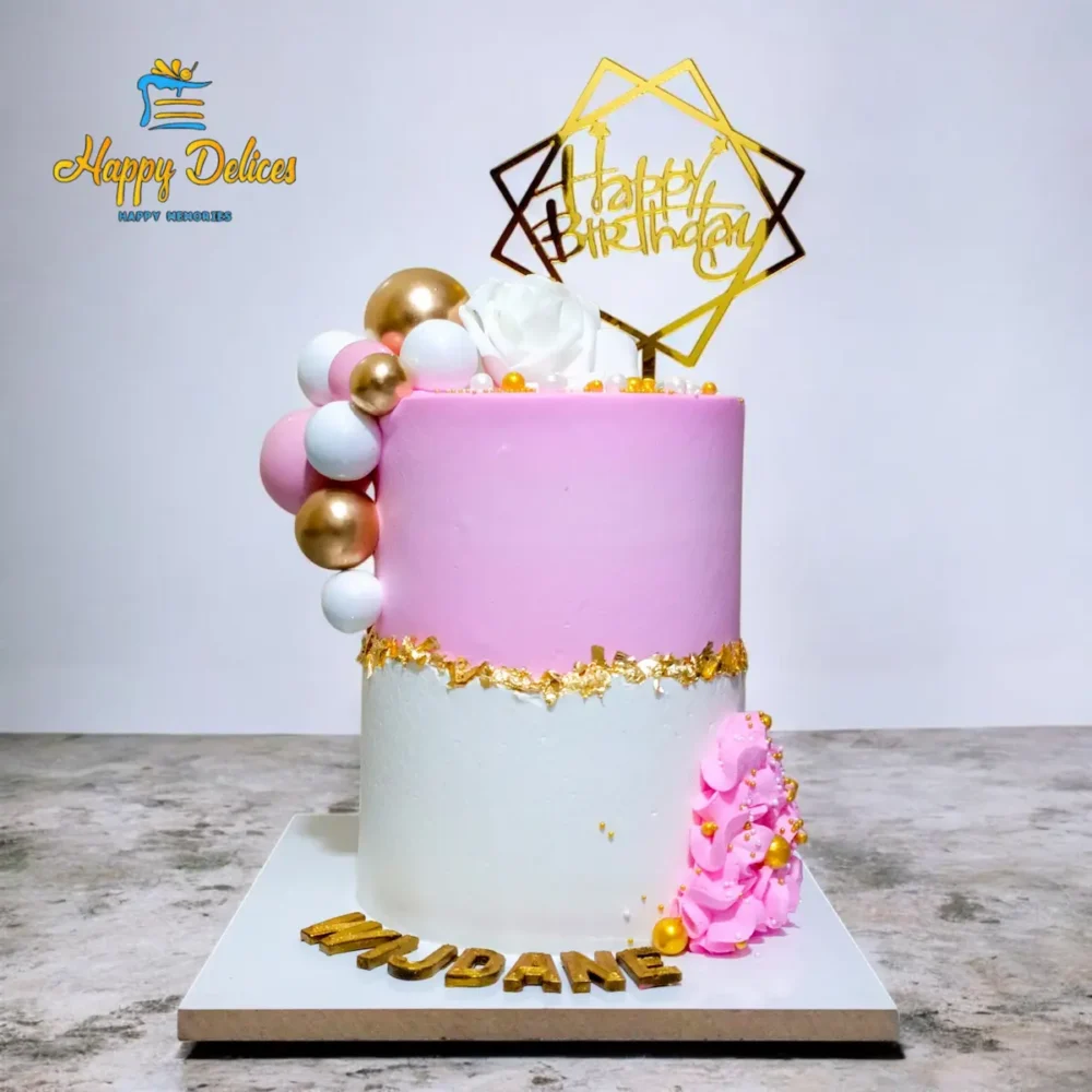 Elegant pink and white birthday cake with gold accents, floral decoration and Happy Birthday topper by Happy Delices